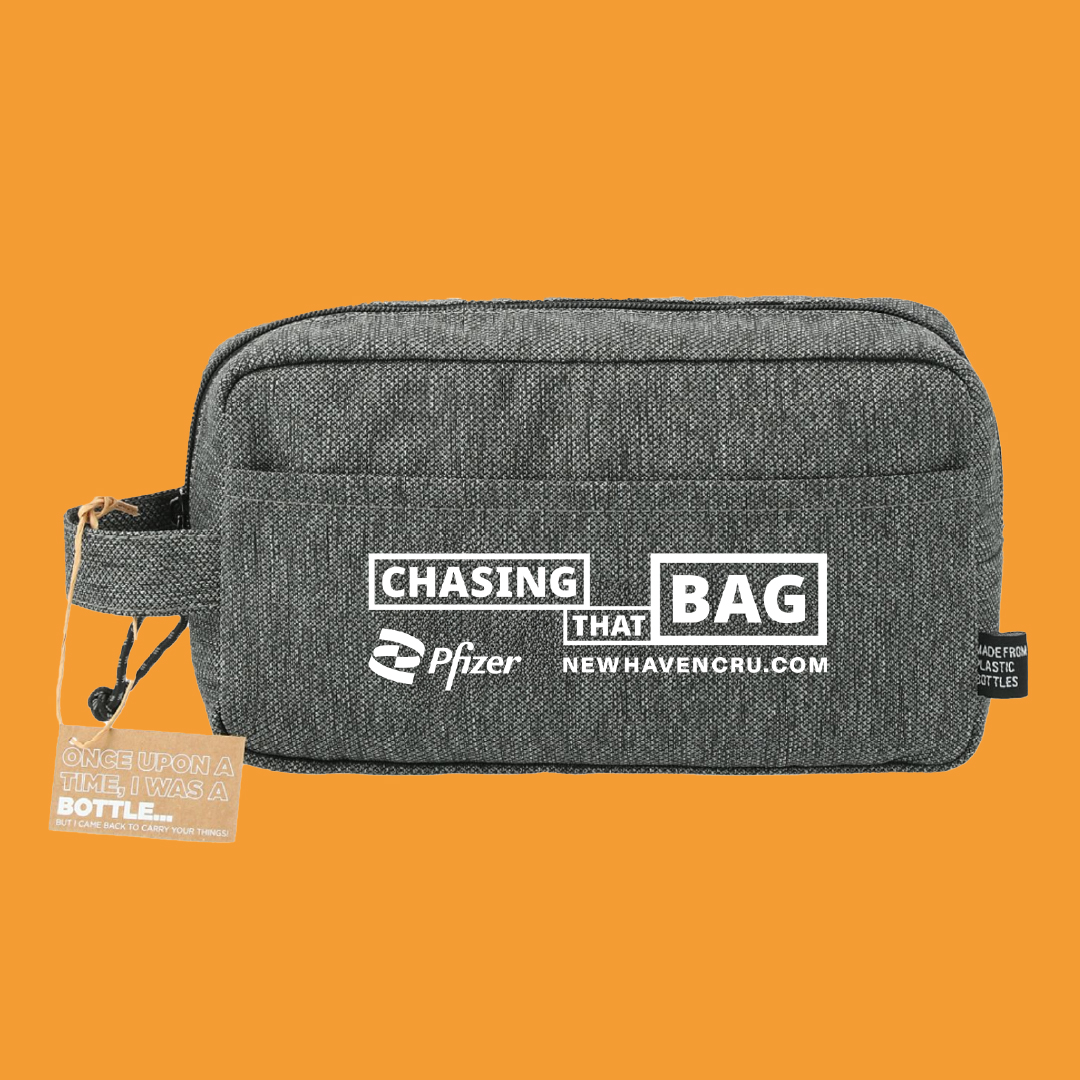 A gray fabric toiletry bag with handle with “Chasing that bag” and “Newhavencru.com” printed on the front pictured on an orange background.