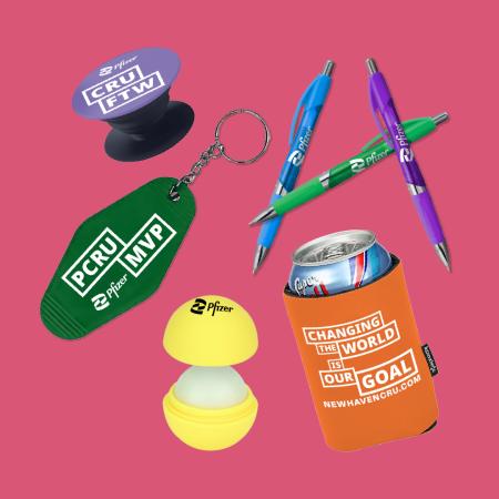A collection of colorful promotional PCRU-branded items such as colored pens, lip balm, and keychains on a bright pink background.
