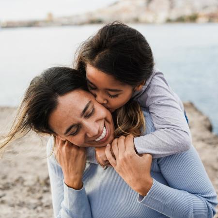 A young child kissing a women’s cheek while embracing them from behind – Pfizer Clinical Trials