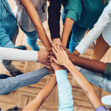 A group of healthy volunteers stack their hands on top of each other while standing in a circle